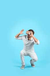 Young man using cardboard virtual reality headset on color background