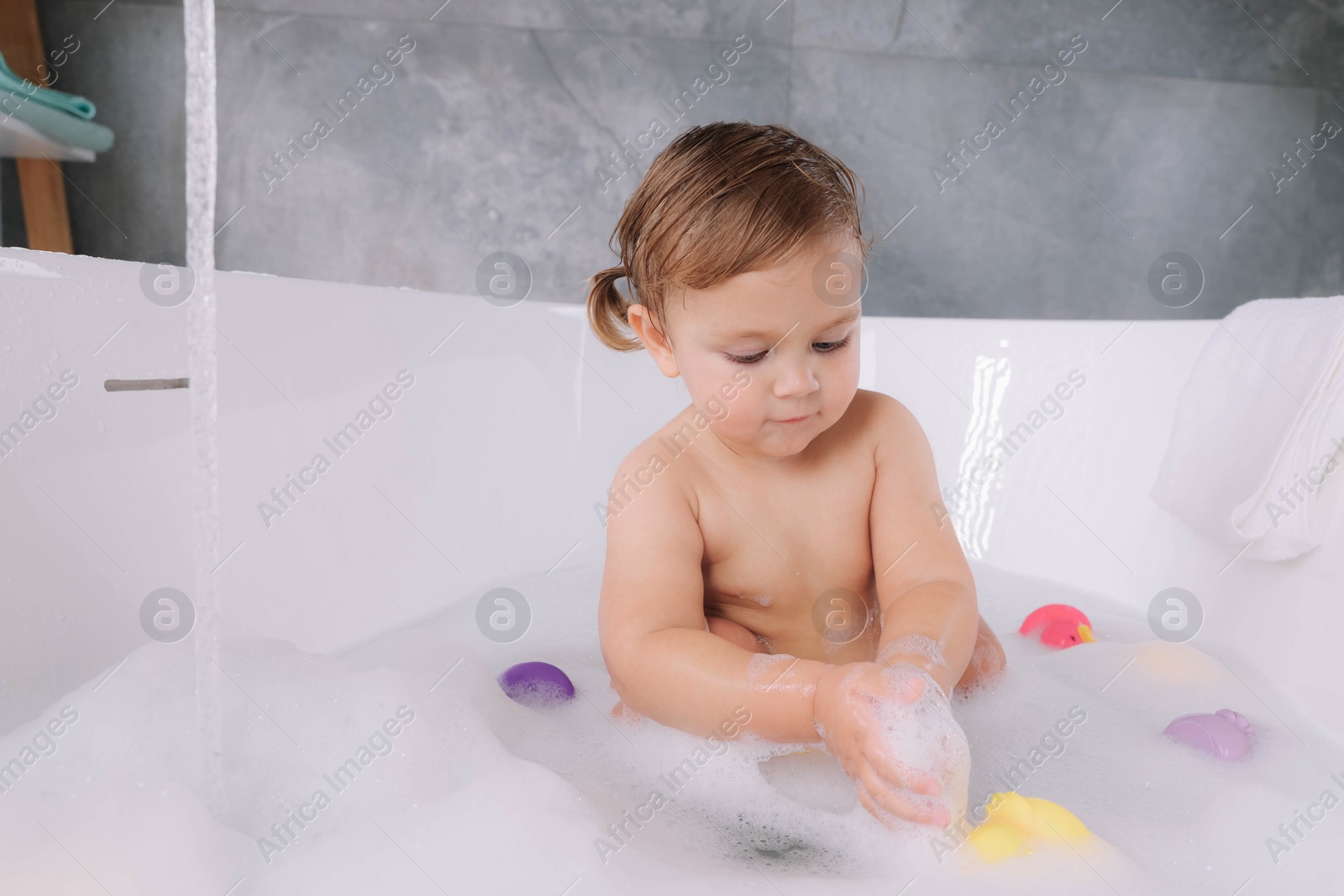 Photo of Cute little girl taking bubble bath with toys indoors