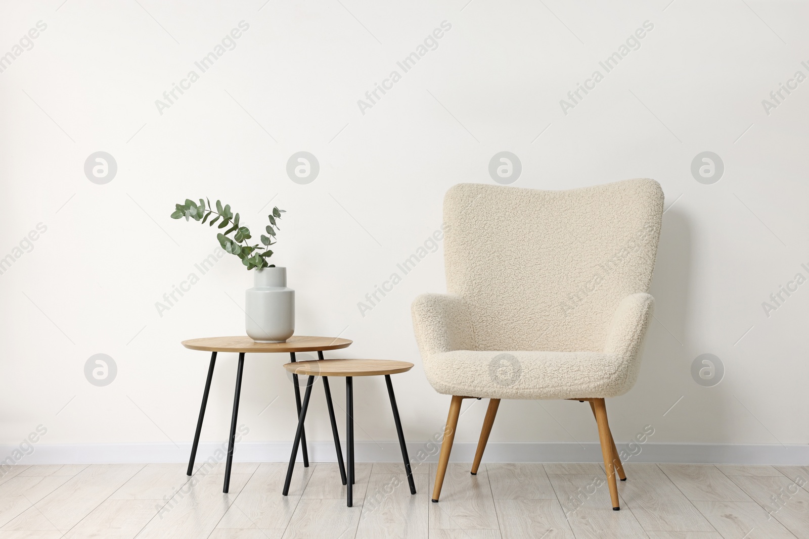 Photo of Comfortable armchair, nesting tables and eucalyptus indoors