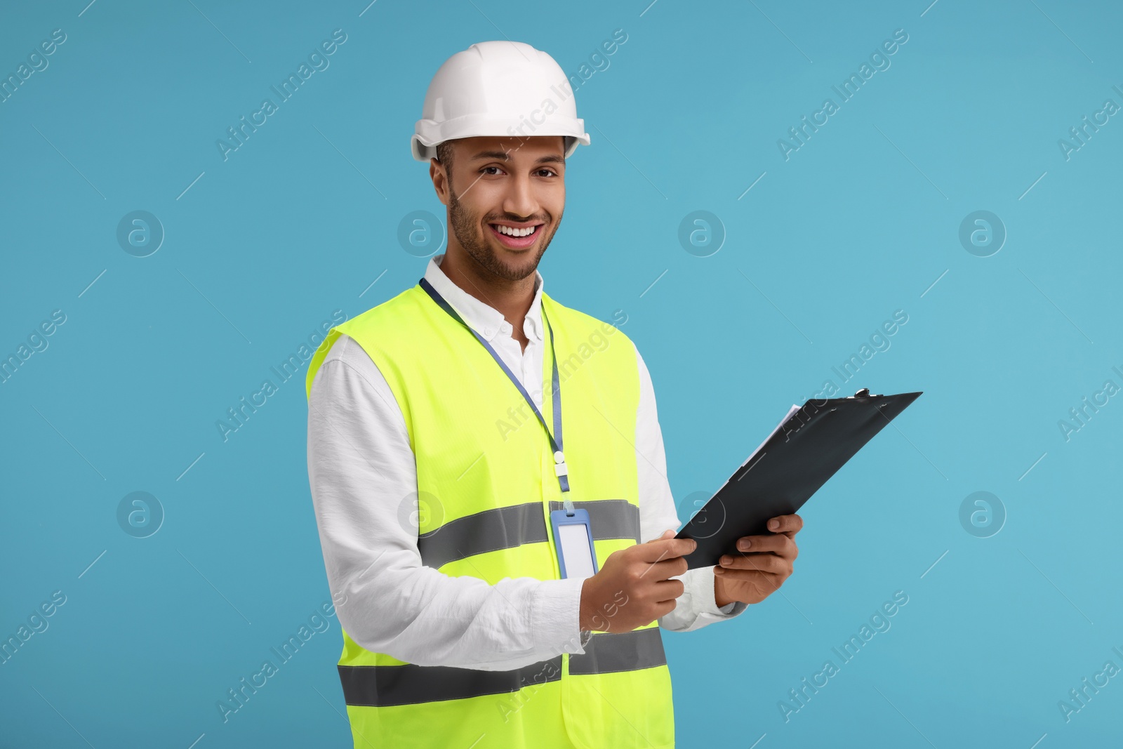 Photo of Engineer in hard hat holding clipboard on light blue background