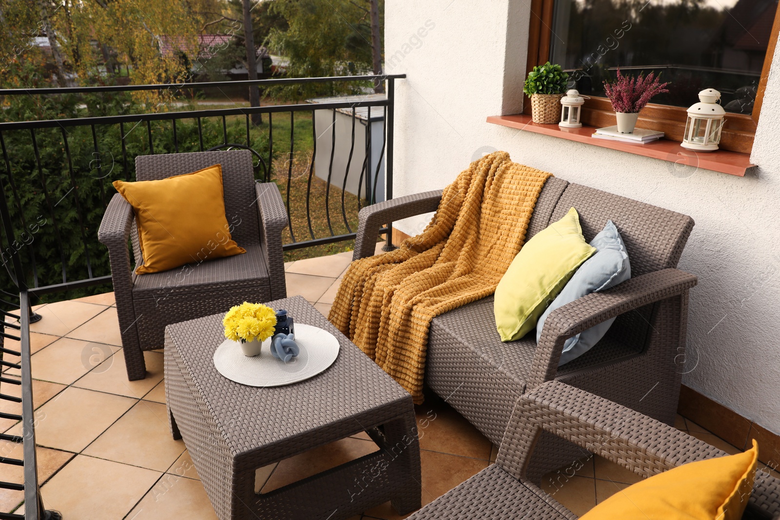 Photo of Colorful pillows, soft blanket and yellow chrysanthemum flowers on rattan garden furniture outdoors