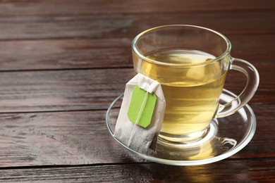 Photo of Tea bag and glass cup of hot beverage on wooden table, space for text