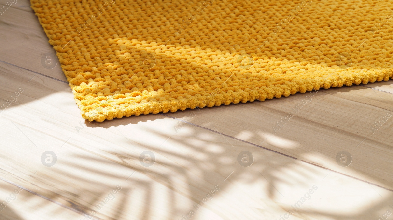 Photo of Soft mustard color bath mat on wooden floor indoors, closeup