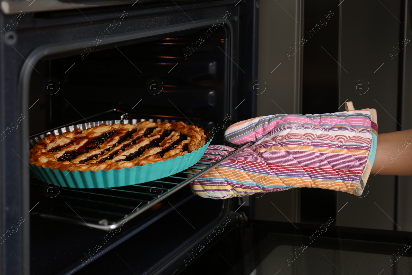 Photo of Woman taking delicious fresh homemade cake out of oven indoors, closeup