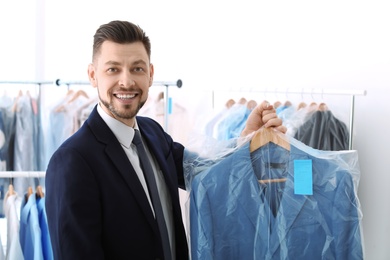 Young businessman holding hanger with jacket in plastic bag at dry-cleaner's