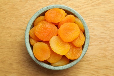 Photo of Bowl of tasty apricots on wooden table, top view. Dried fruits