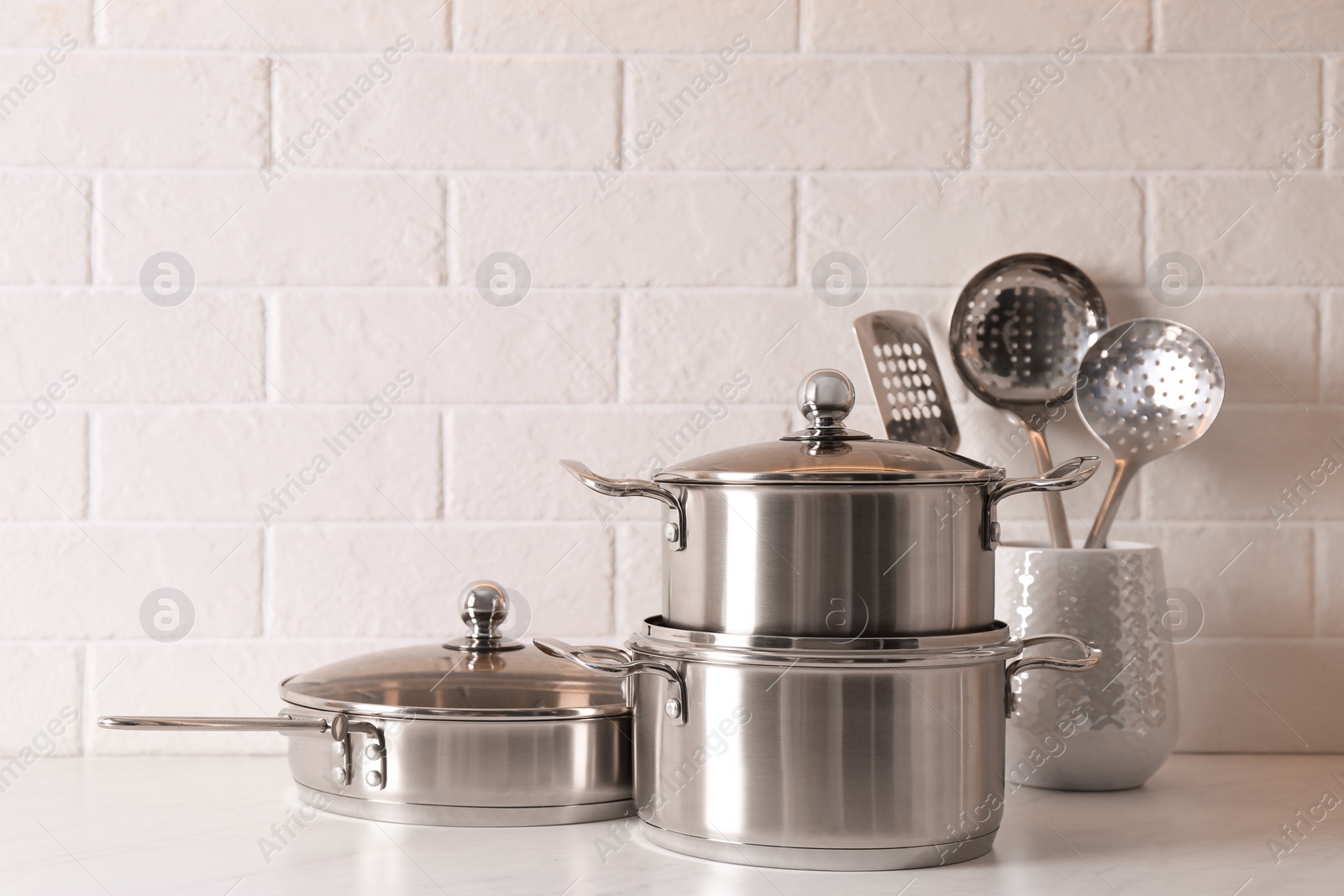 Photo of Set of stainless steel cookware and kitchen utensils on table near white brick wall, space for text