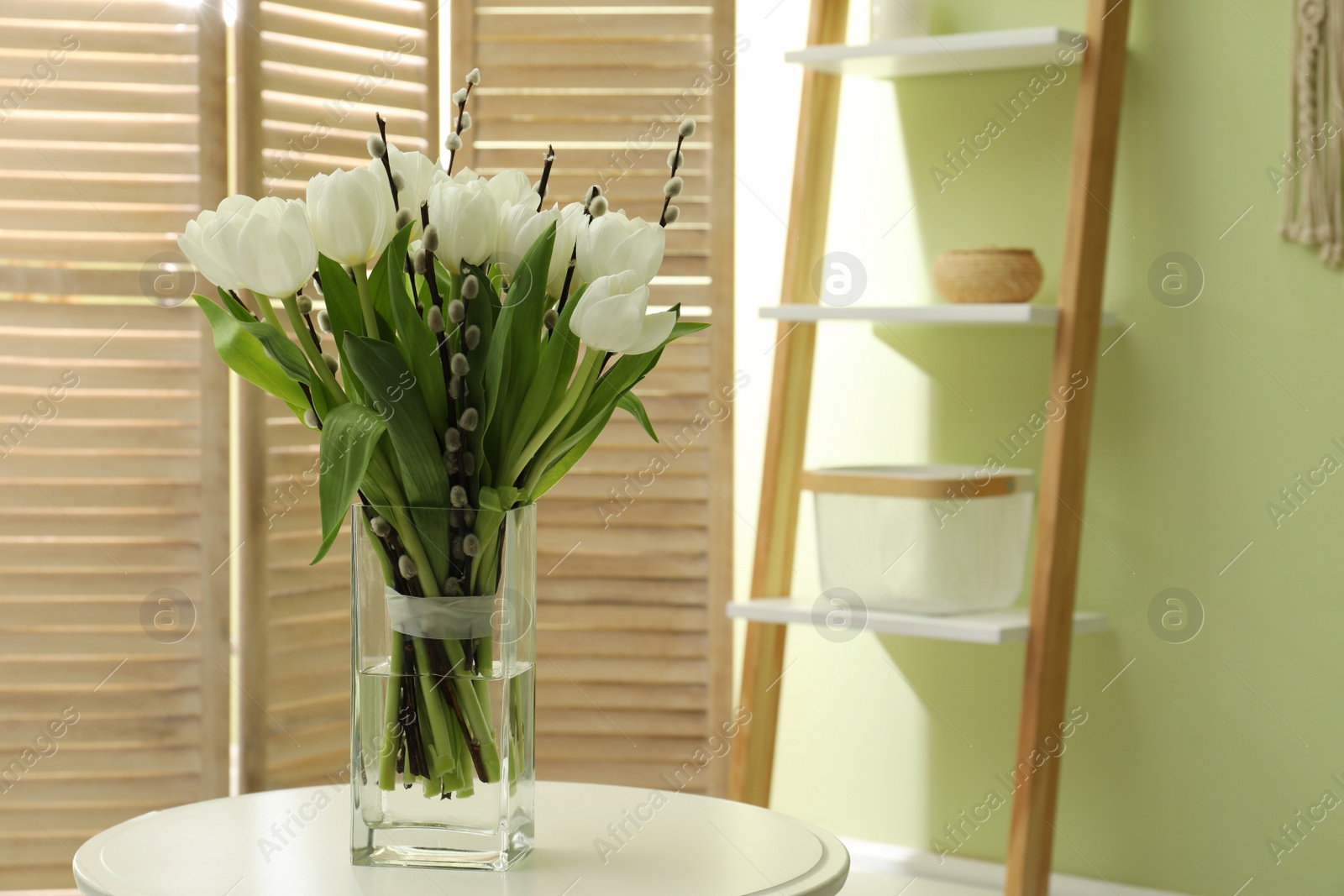 Photo of Beautiful bouquet of willow branches and tulips in vase on table indoors, space for text