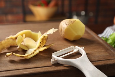 Photo of Wooden board with potato, peels and peeler on table, closeup