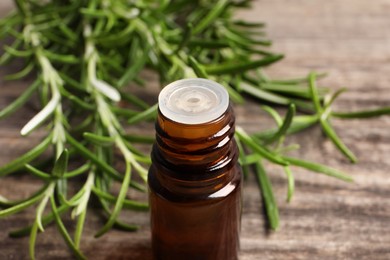 Bottle of essential oil and fresh rosemary sprigs on table, closeup