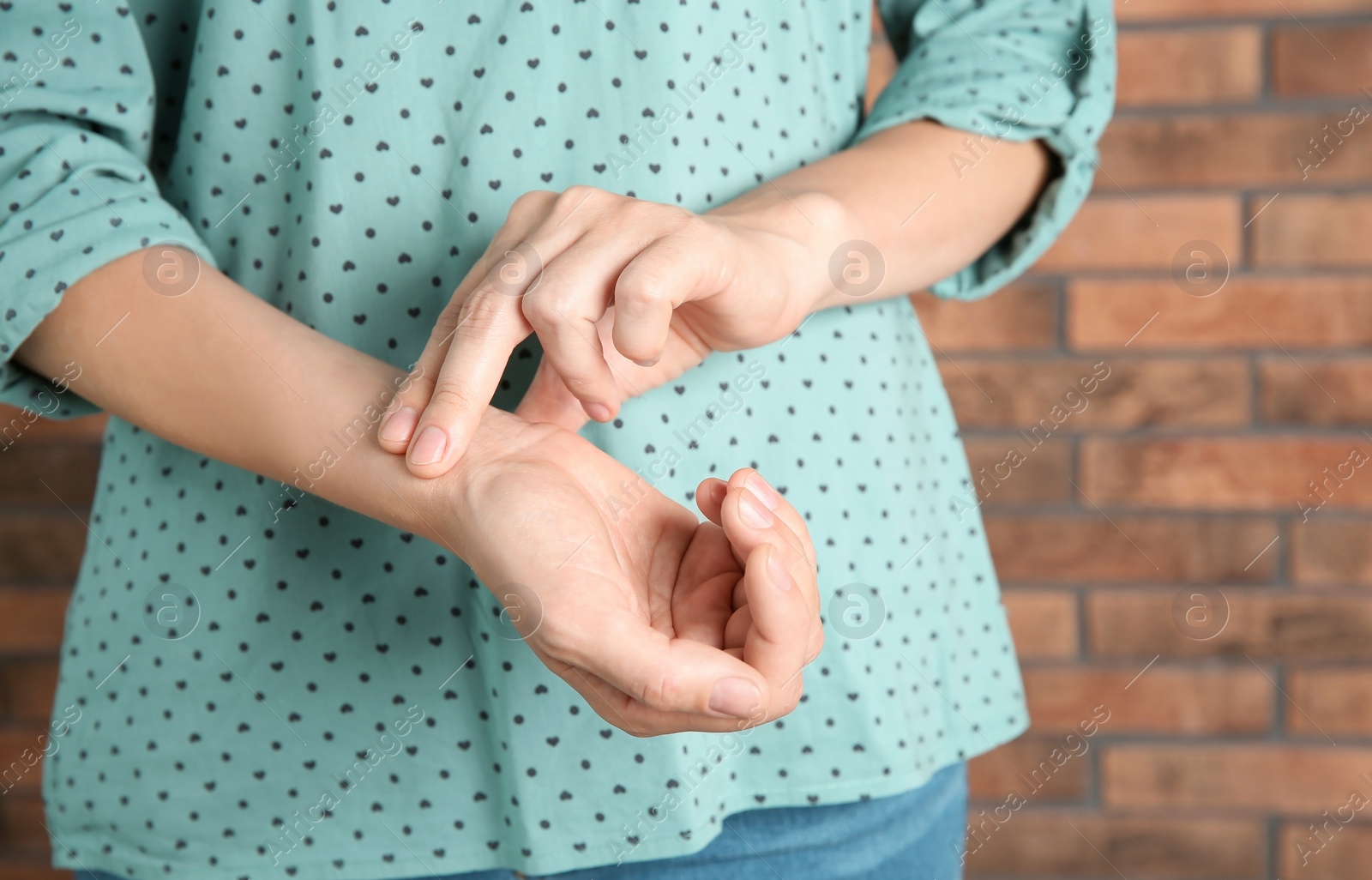 Photo of Young woman checking pulse on brick wall background