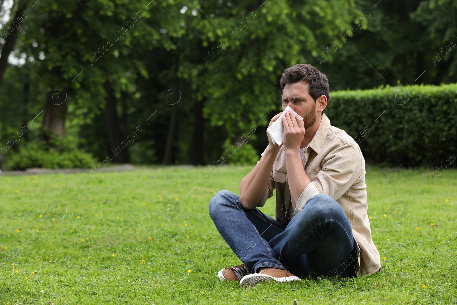 Photo of Man suffering from seasonal spring allergy on green grass in park. Space for text