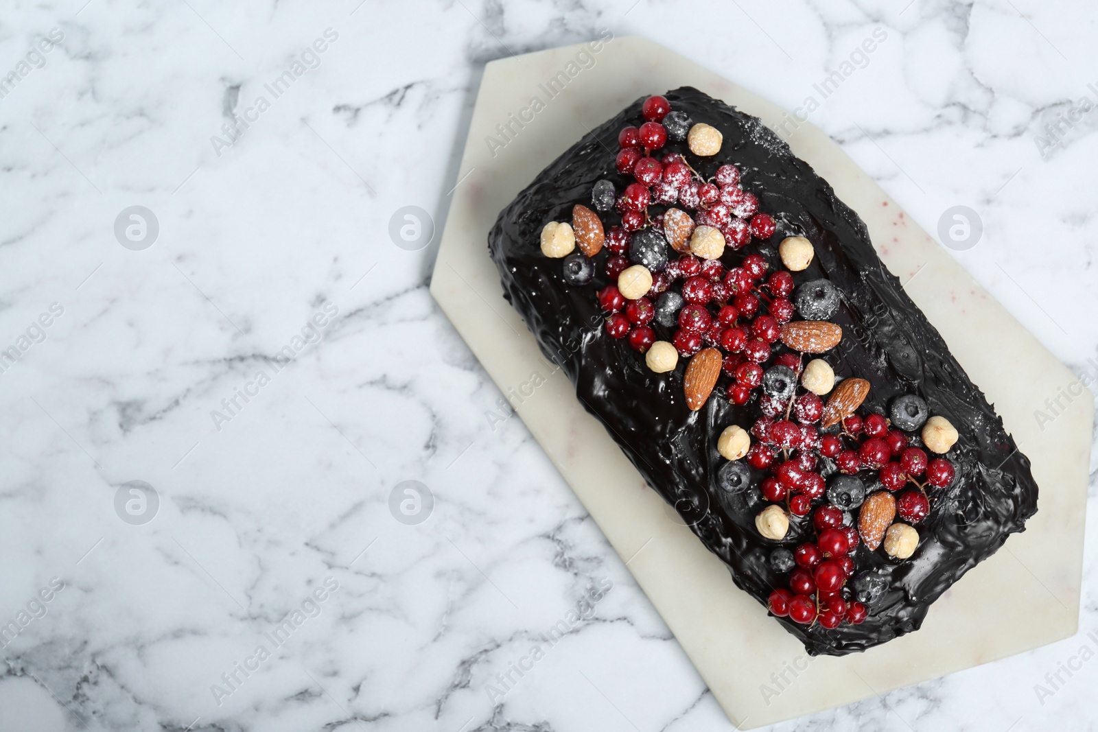 Photo of Delicious chocolate sponge cake with berries and nuts on white marble table, top view. Space for text