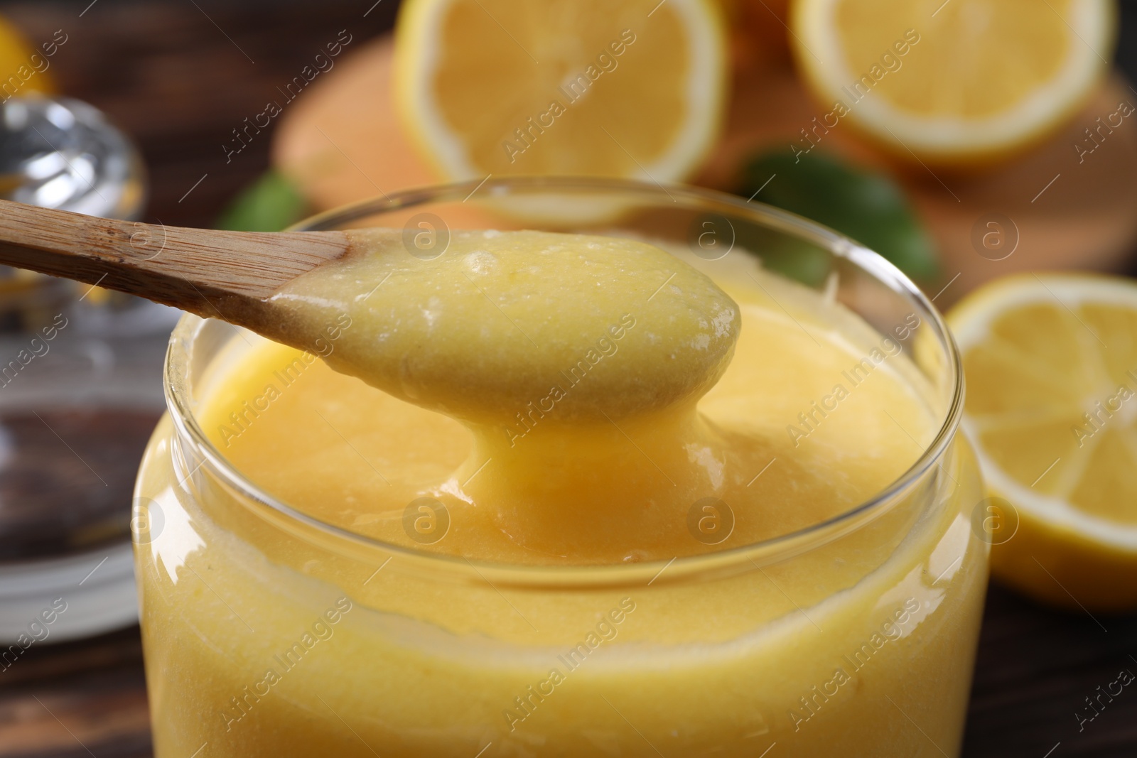 Photo of Taking delicious lemon curd from glass jar at table, closeup