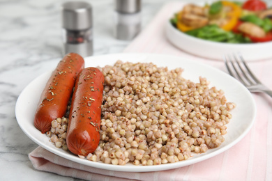 Photo of Tasty buckwheat porridge with sausages on white marble table