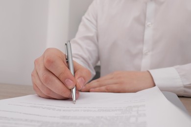 Photo of Man signing document at table, closeup view