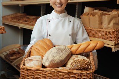 Photo of Professional baker with tray full of fresh breads in store, closeup