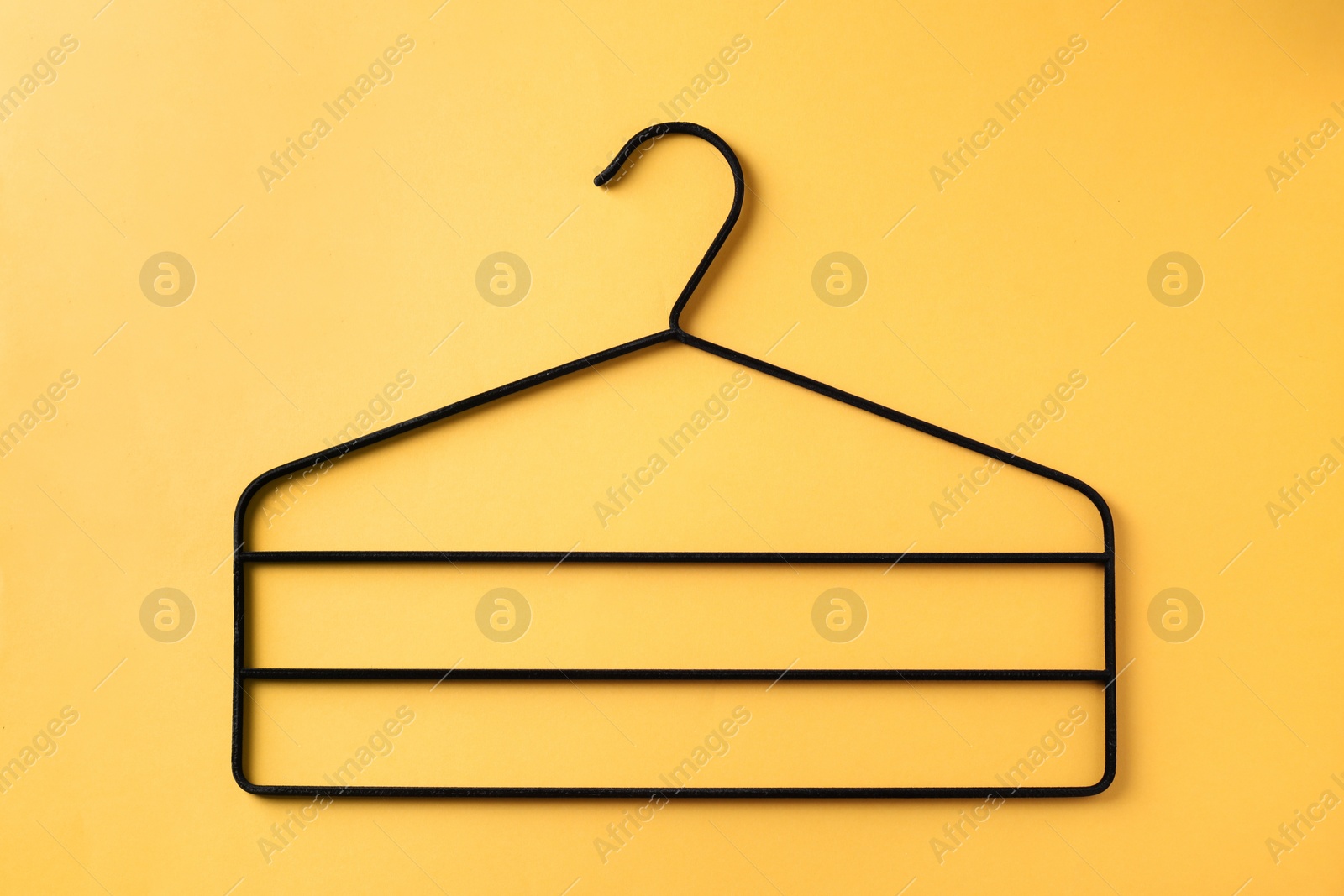 Photo of One black hanger on yellow background, top view