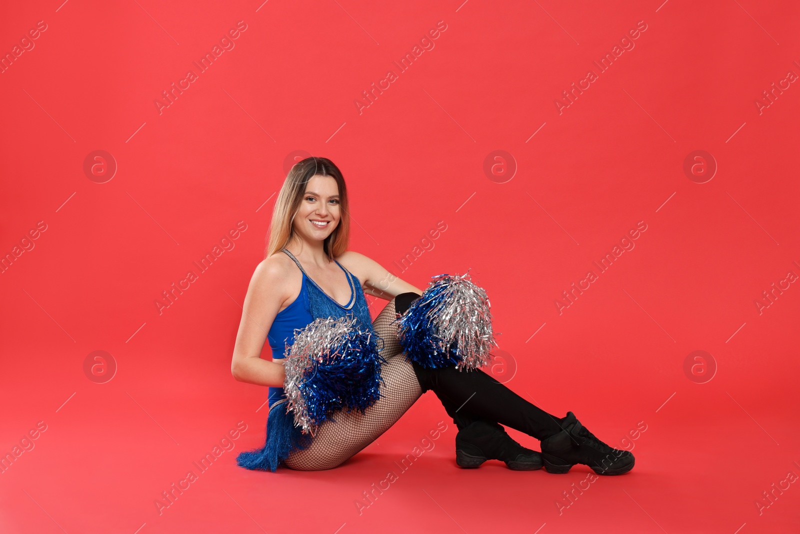 Photo of Beautiful cheerleader in costume holding pom poms on red background