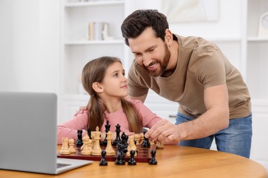 Father teaching his daughter to play chess following online lesson at home