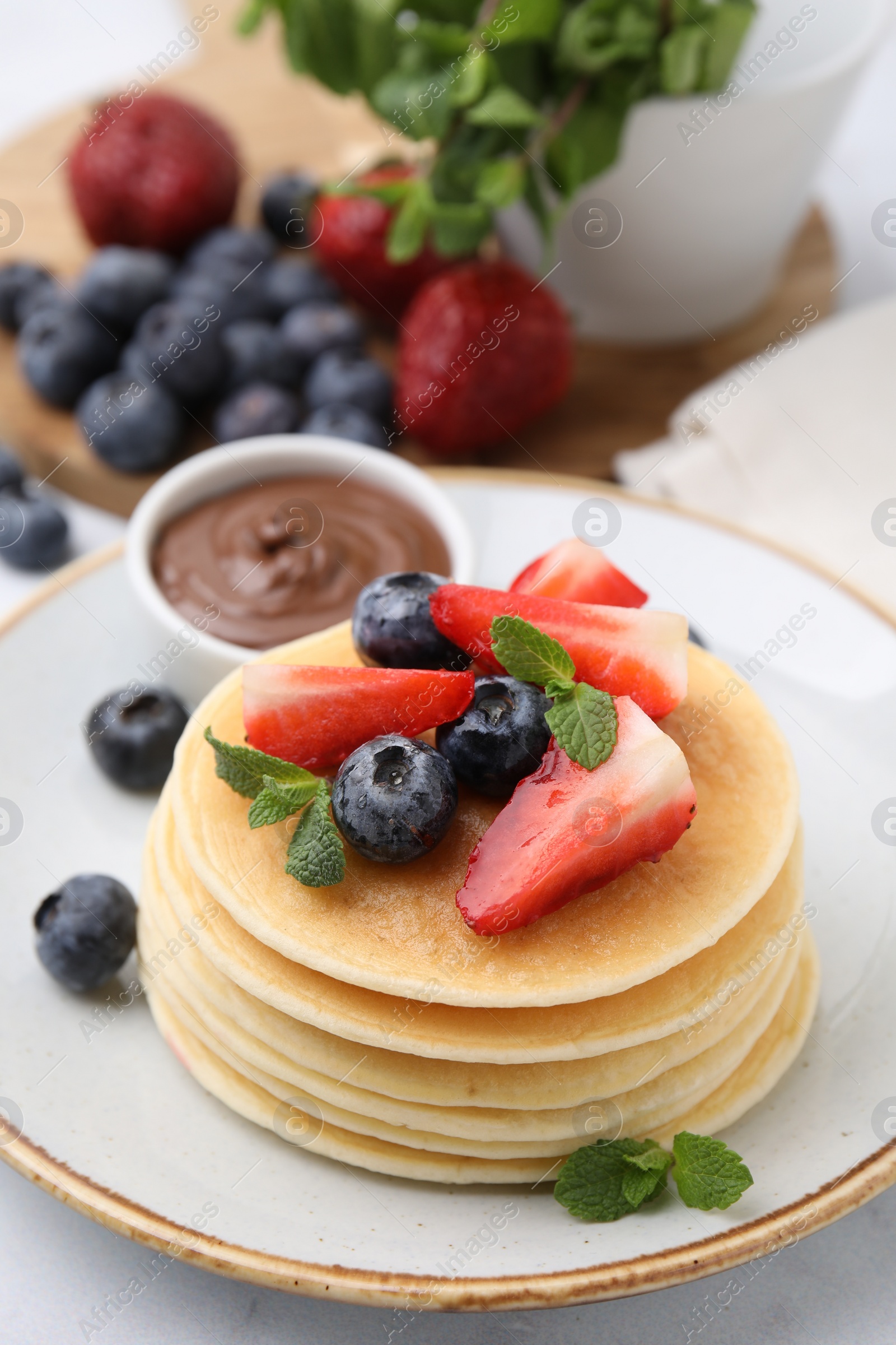 Photo of Delicious pancakes with strawberries, blueberries and chocolate sauce on table, closeup