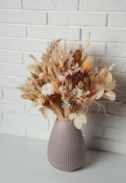 Beautiful dried flower bouquet in ceramic vase on table near white brick wall