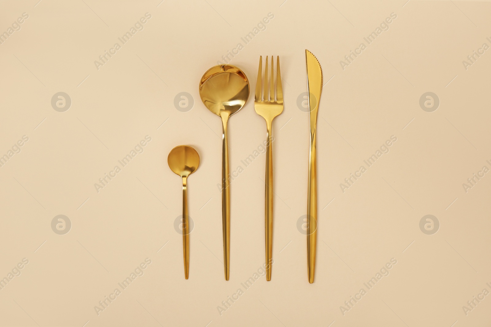 Photo of Stylish golden cutlery set on beige background, flat lay