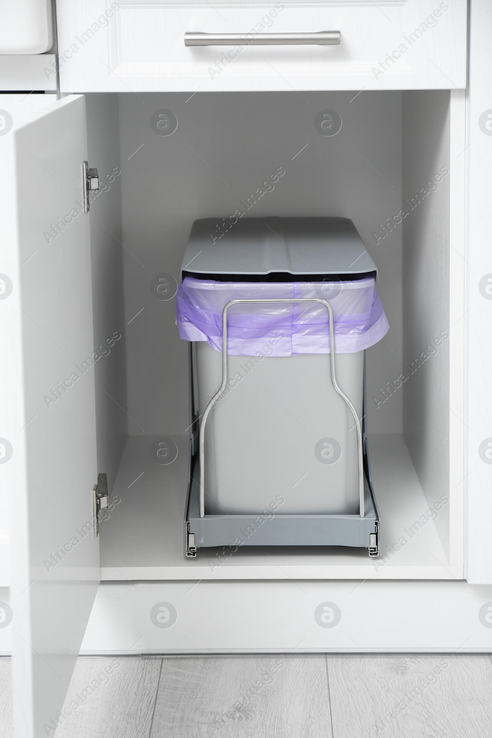 Photo of Open cabinet with trash bin in kitchen