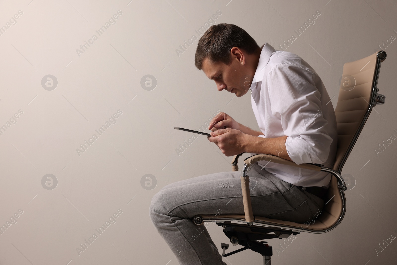 Photo of Man with bad posture using tablet while sitting on chair against grey background. Space for text