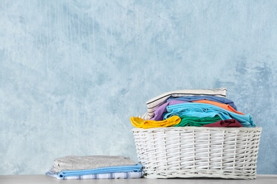 Photo of Basket with clean laundry on table against color background, space for text