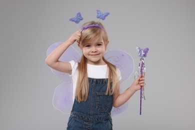 Photo of Cute little girl in fairy costume with violet wings and magic wand on light grey background