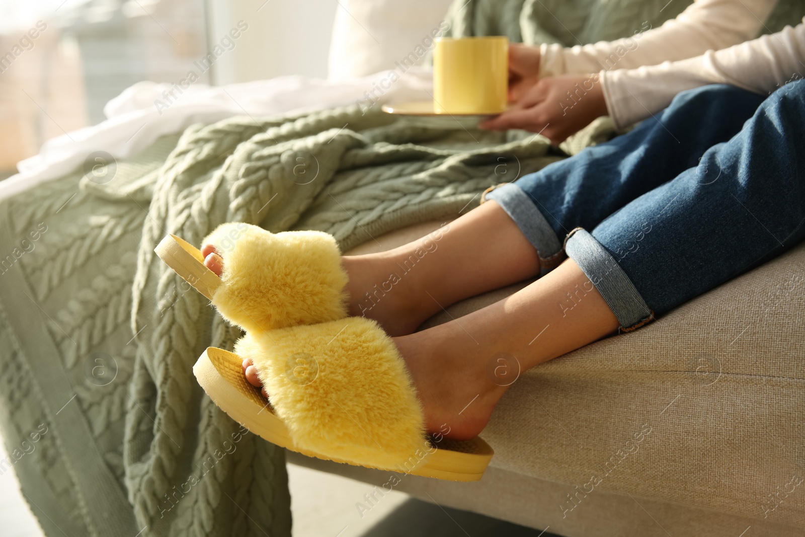Photo of Woman with cup of drink wearing soft comfortable slippers at home, closeup