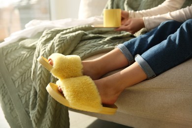 Woman with cup of drink wearing soft comfortable slippers at home, closeup