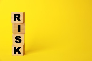 Photo of Word Risk made of wooden cubes on yellow background, space for text