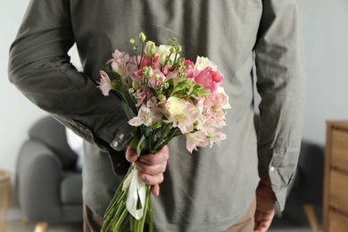 Man hiding bouquet of flowers for his beloved woman indoors, closeup