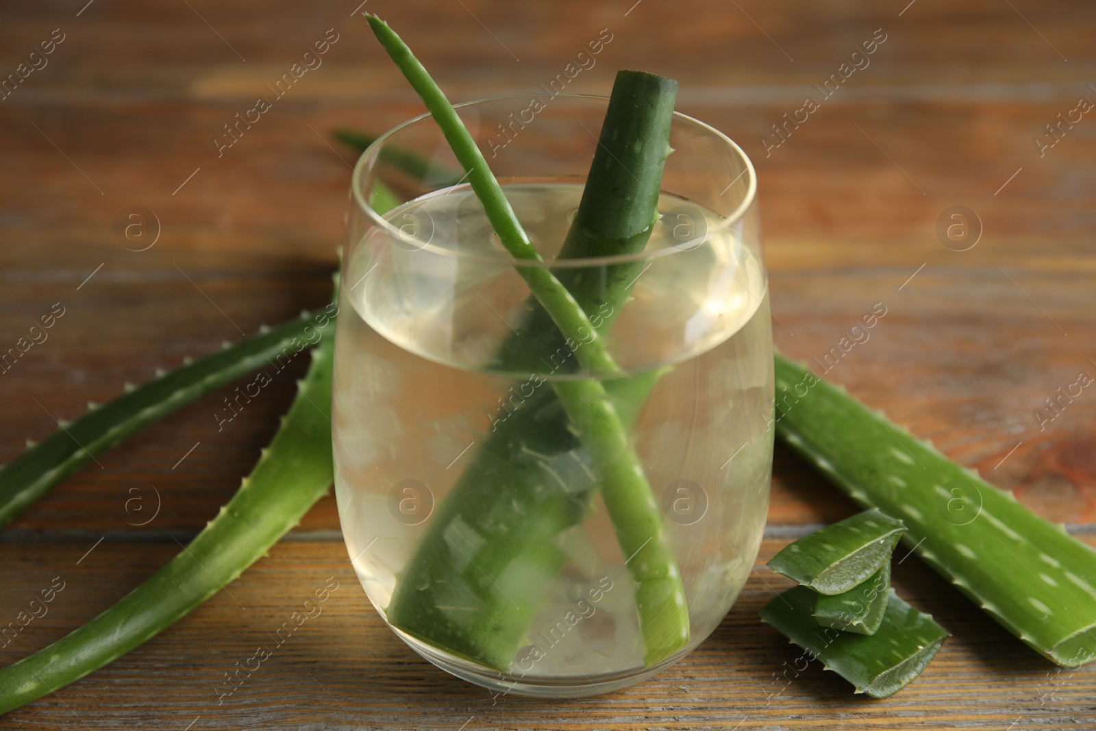 Photo of Fresh aloe drink with leaves in glass on wooden table, closeup