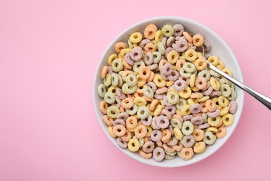 Tasty cereal rings in bowl and spoon on pink table, top view. Space for text