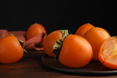 Photo of Tasty ripe persimmons on brown wooden table, closeup