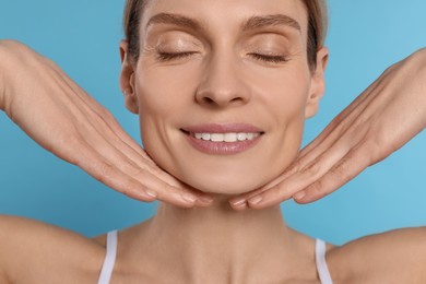 Photo of Woman massaging her face on turquoise background