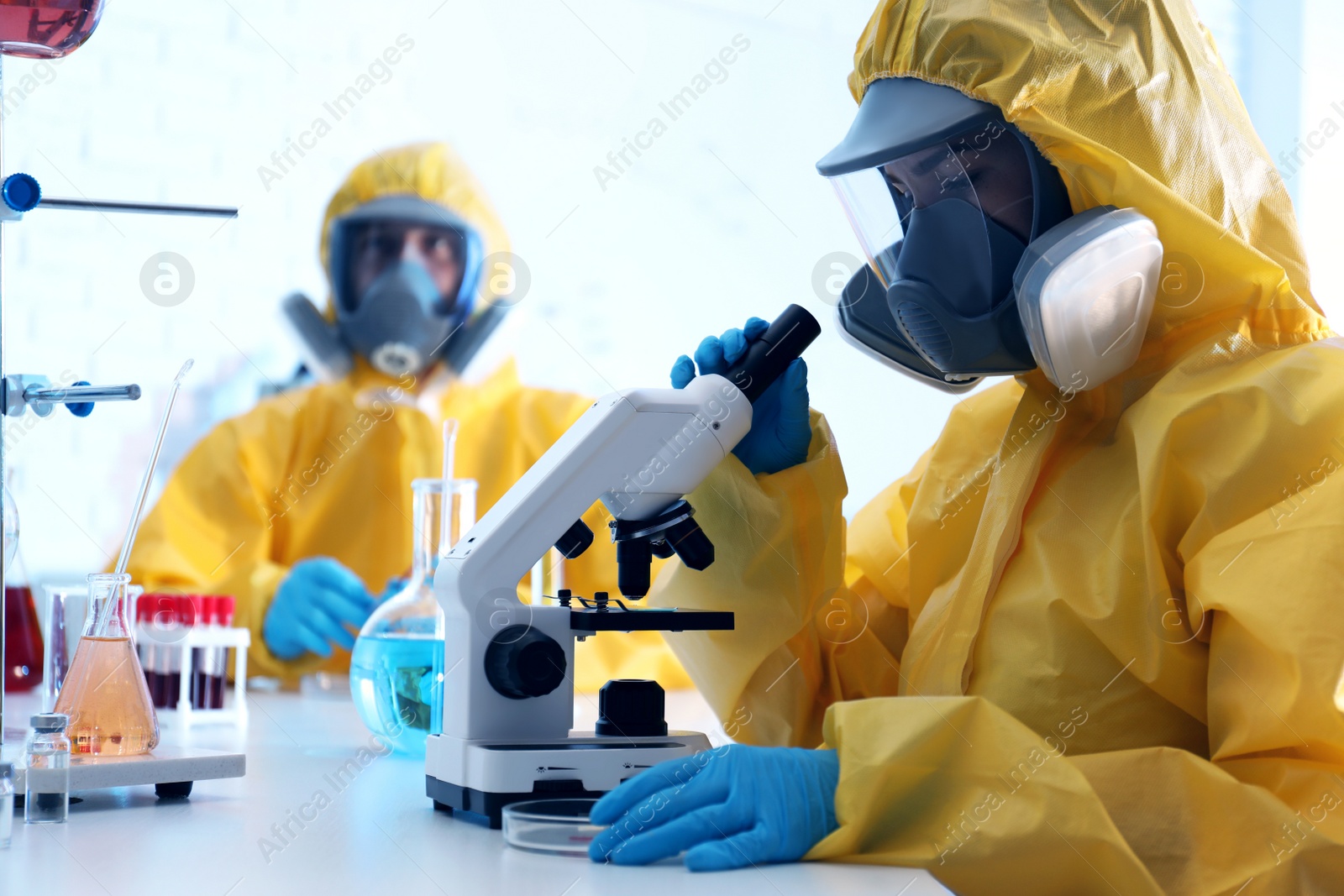 Photo of Scientist in chemical protective suit using microscope at laboratory. Virus research