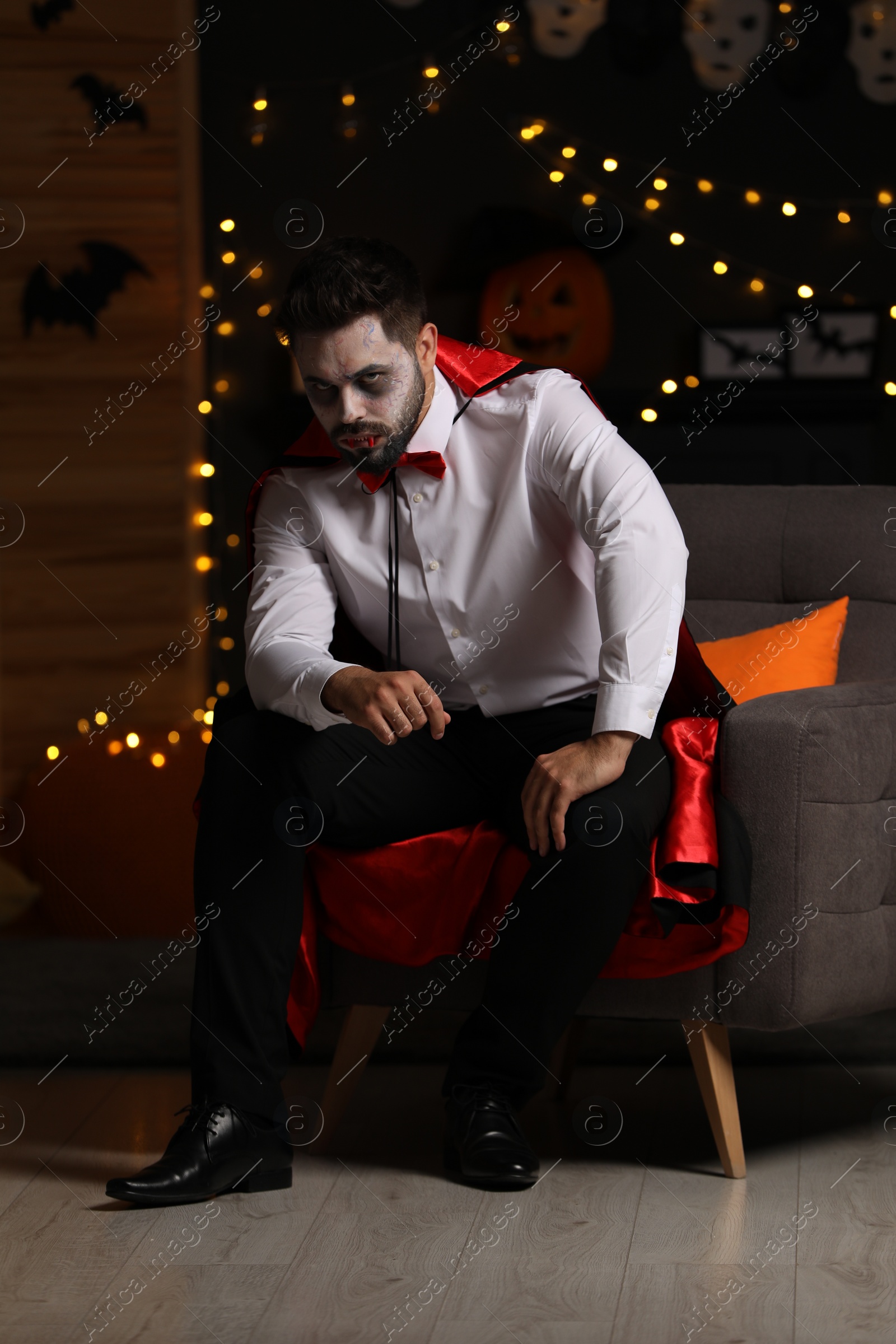 Photo of Man in scary vampire costume against blurred lights indoors. Halloween celebration