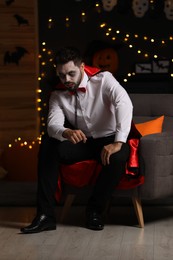 Man in scary vampire costume against blurred lights indoors. Halloween celebration