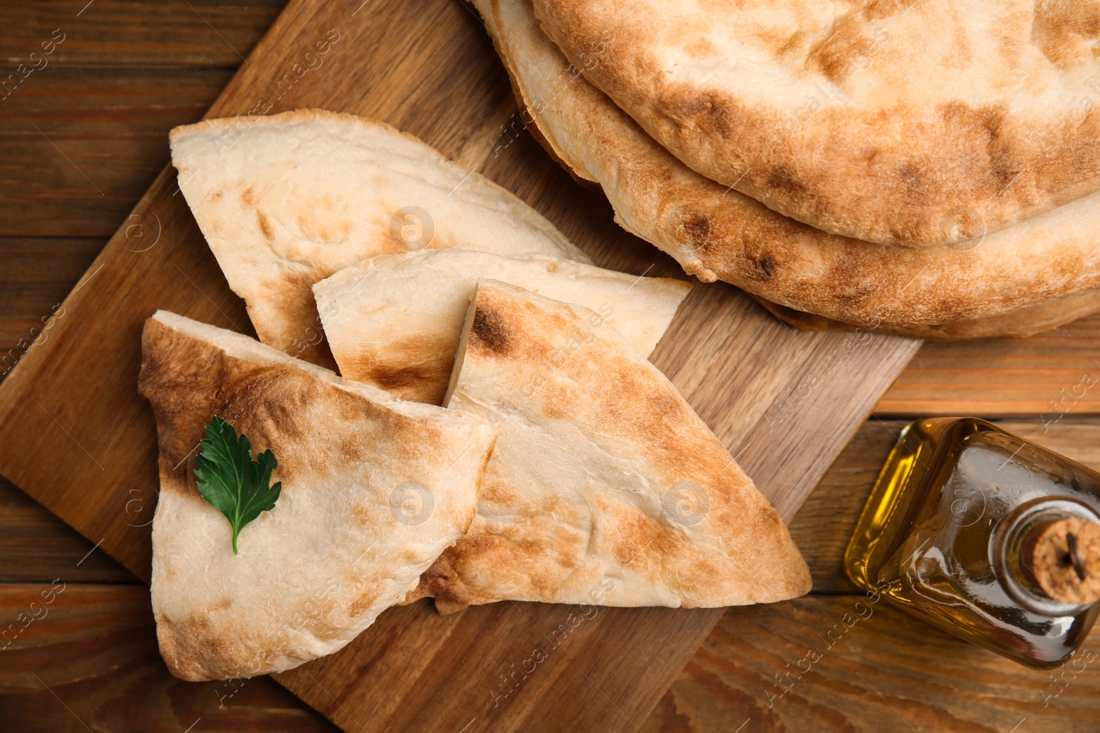 Photo of Cut fresh pita bread and olive oil on wooden table, top view