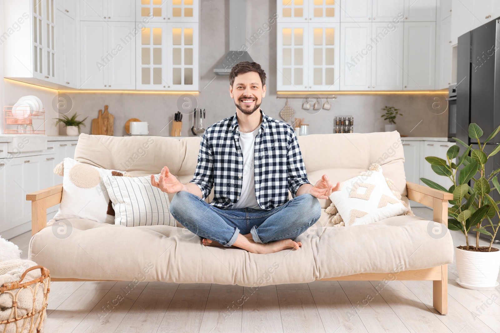 Photo of Happy man meditating on sofa at home. Harmony and zen