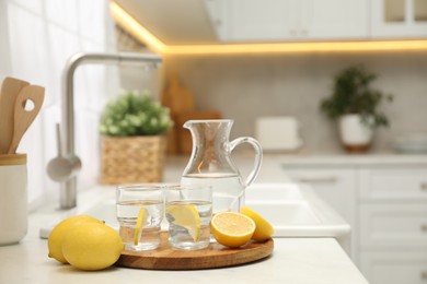 Photo of Jug, glasses with clear water and lemons on white table in kitchen, space for text