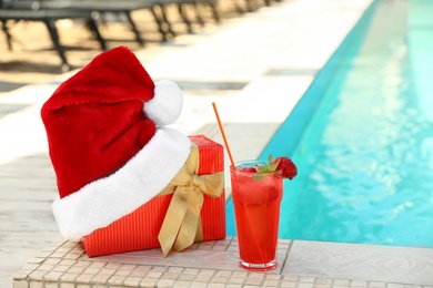 Photo of Authentic Santa Claus hat, gift box and cocktail near pool at resort