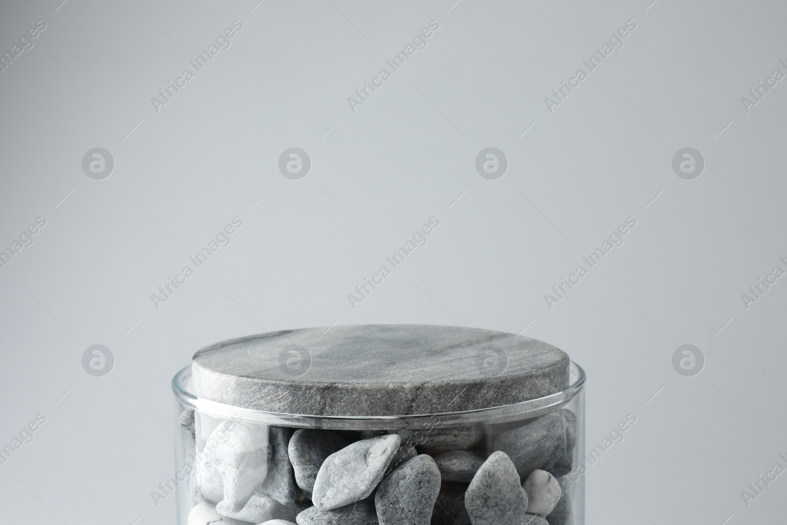 Photo of Presentation for product. Glass container with stones on light grey background. Space for text