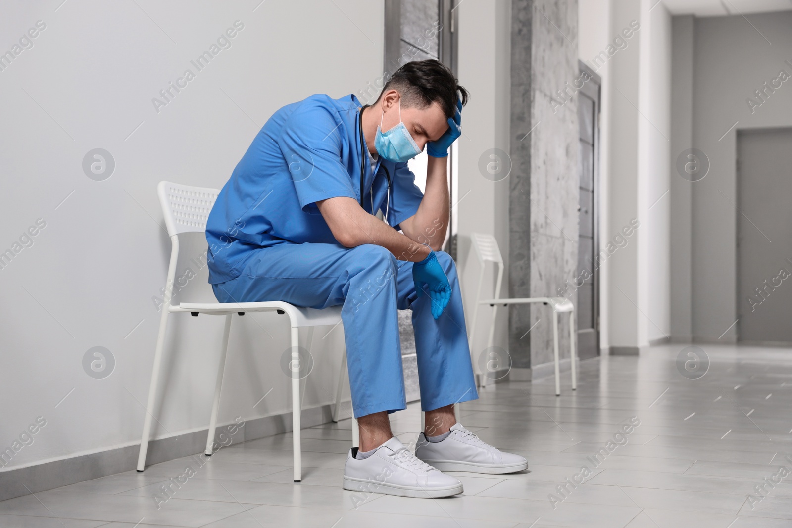 Photo of Exhausted doctor sitting on chair in hospital hallway