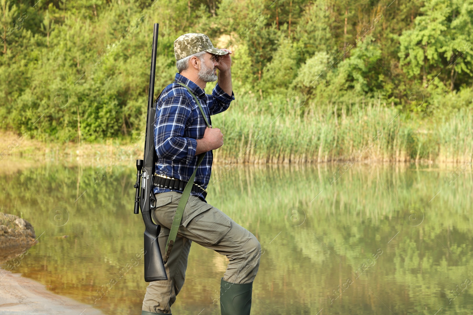 Photo of Man with hunting rifle near lake outdoors. Space for text