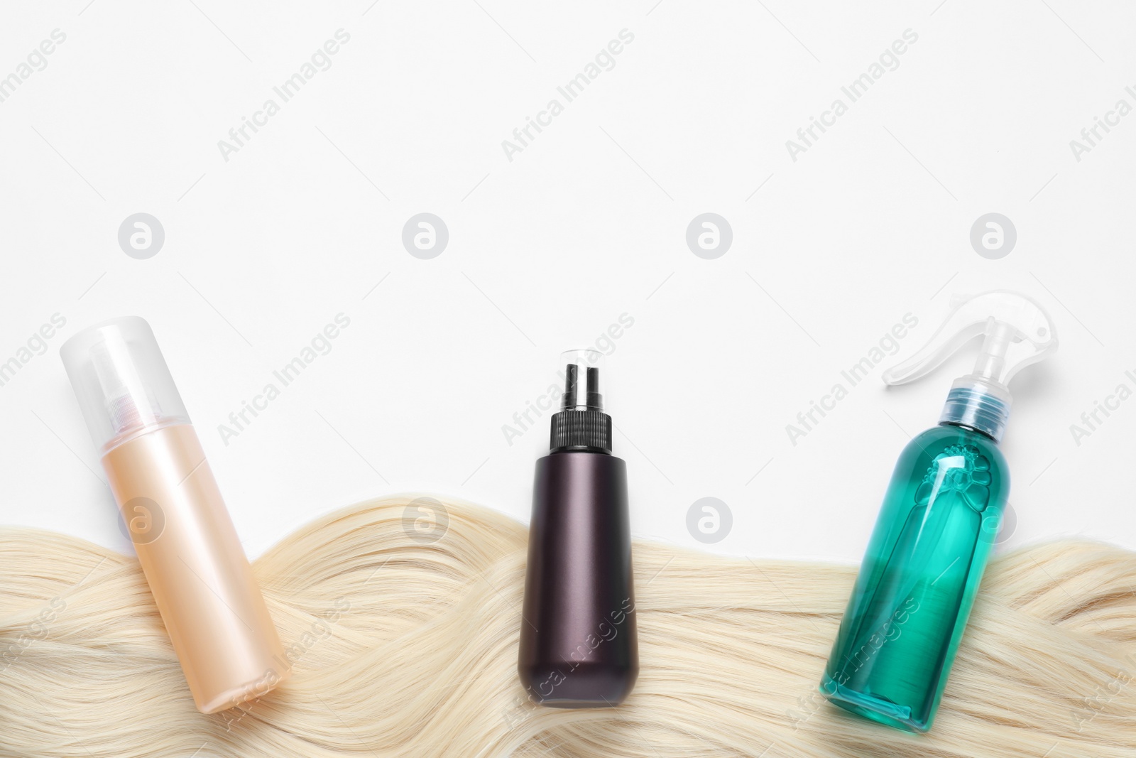 Photo of Spray bottles with thermal protection and lock of blonde hair on white background, flat lay. Space for text